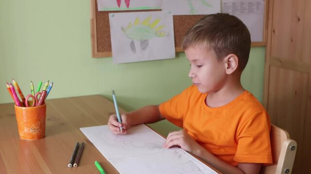 Boy drawing dinosaurs sitting by desk in kids room