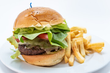 Huge cheeseburger plate served with french fries is stacked tall with lettus and homemade bun.