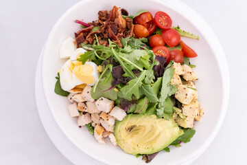 Overhead view of cobb salad piled high with sliced avocado, tomato, chicken, hard boiled egg, and arrugula