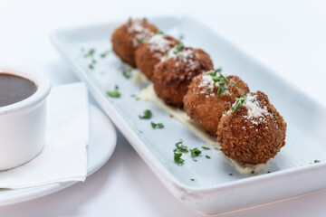 Parmesan topped Risotto Arancinis Italian meatballs lined up on a rectangular plate served with dipping sauce.