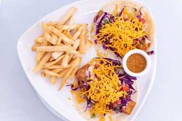 Overhead view of combo plate of fish tacos topped with shredded cheese served with french fries and salsa