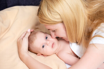 Portrait of Young Caucasian Mother Embracing Her Newborn Baby Boy Lying on Bed.