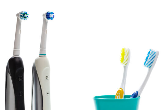 Closeup of Two Professional Electric Toothbrushes In Front of Two Manual Tooth Brushes in One Cup