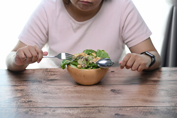 Cropped shot of overweight woman is tired of diet restrictions eating green salad sitting at table.