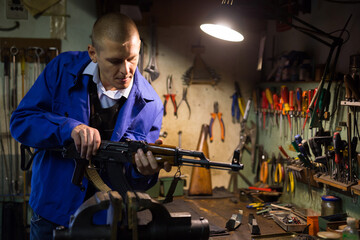 Obraz na płótnie Canvas Qualified gunsmith performing maintenance of Kalashnikov assault rifle in weapons workshop.