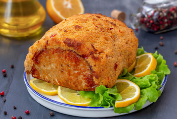Sunday Pork Roast. Spicy Oven baked meat in breadcrumb crust with lemon, herb and chili on white plate.  Dark wooden background.