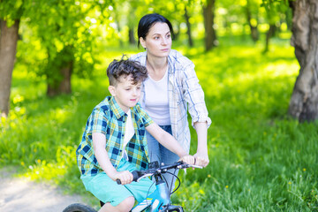 Mom pushes sfn on a bicycle so that he learns to ride. Mom and son relationship concept. Place for text