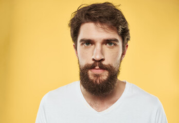 A man with a beard and mustache on a yellow background and a white T-shirt