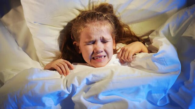 top view. A sweet little girl naps in bed, sees a nightmare and fears in sleep