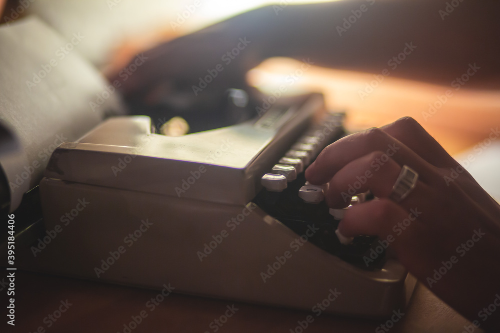 Fototapete Process of writing a text letter on a white sheet of paper with old-fashioned typewriter, modern writer machine in warm room light, close up view of hands writing and printing