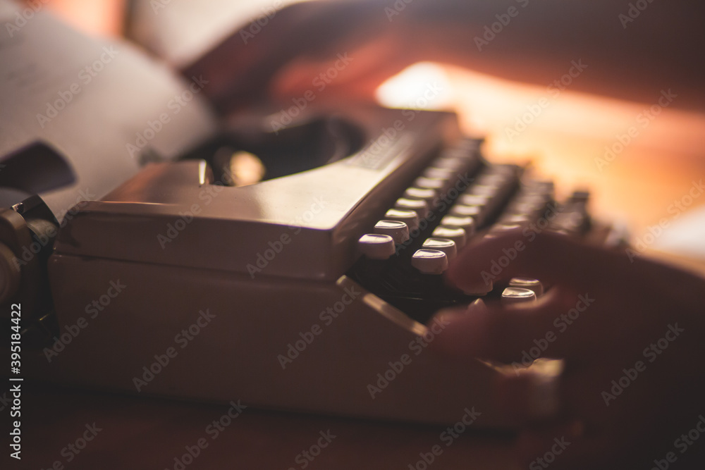 Fototapete Process of writing a text letter on a white sheet of paper with old-fashioned typewriter, modern writer machine in warm room light, close up view of hands writing and printing