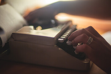 Process of writing a text letter on a white sheet of paper with old-fashioned typewriter, modern writer machine in warm room light, close up view of hands writing and printing