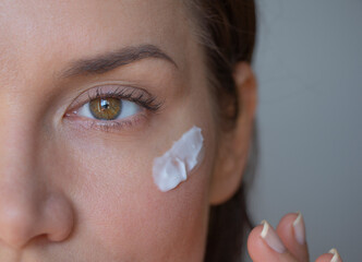
An older girl applies an evening cream for mimic wrinkles under her eyes