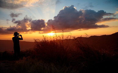 Obraz premium man taking photo of beautiful sunset on top mountain