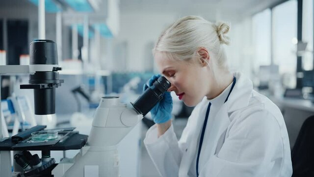 Modern Medical Research Laboratory: Portrait of Female Scientist Looking Under Microscope, Analysing Biochemicals Samples. Advanced Scientific Lab for Medicine, Microbiology Development
