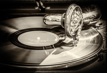 Old gramophone plays an old vinyl record. Old style black and white photo in sepia.