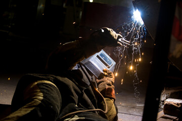 A welder is welding a metal pipe with electric welding. Electric welder repairs a pipe in a workshop