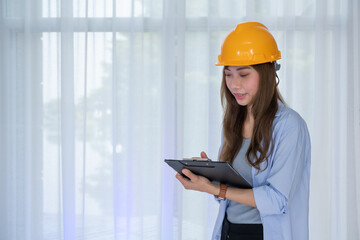 Female Engineer wear face mask with safety yellow helmet standing inside building check the...
