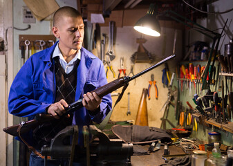 Experienced craftsman of weapons workshop inspecting semi-automatic hunting shotgun before repair