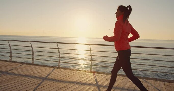 Beautiful caucasian young woman running along the alley over sea on background of sunlight. Morning run. Healthy Lifestyle.