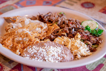 Exquisite traditional Mexican chilaquiles with machaca accompanied by beans with cheese on top.