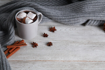Cup of chocolate with marshmallow, spices, grey knitted scarf on white wooden table background. Winter drink concept. Spicy cocoa, menu, high angle, closeup, copy space