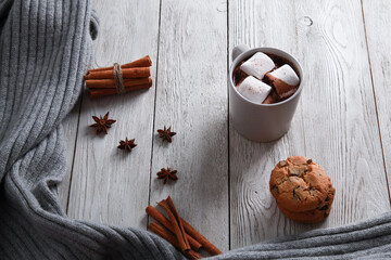 Pale cup of chocolate with marshmallow, spices, cookies, grey knitted plaid on white wooden table background. Winter drink concept. Spicy cocoa, menu, closeup, copy space