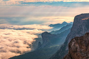 A majestic view of the rocky mountains and the valley in fog and clouds. Creamy fog covered the mountain valley in sunset light. Picturesque and gorgeous scene. Misty sunset over Crimea Mountains