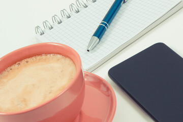 Smartphone, coffee with milk and notepad for writing notes. Work or relaxation with mobile phone. White background