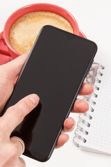Hand of woman with mobile phone, coffee with milk and notepad for writing notes. White background
