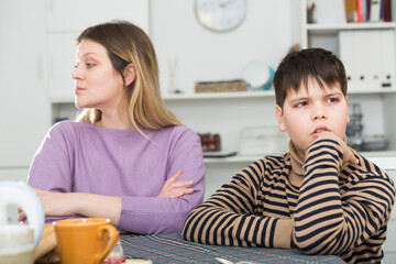 Upset mother and unhappy son sitting after quarrel in domestic interior