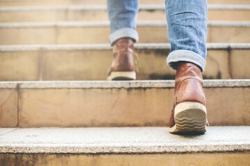 Close up image of young hipster wearing blue jeans and shoes leather walking at city stairs during travel destination to grow and learn experience.