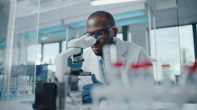Modern Medical Research Laboratory: Portrait of Male Scientist Looking Under Microscope, Writing Down Information