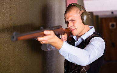 Portrait of confident shooter sighting in or zeroing shotgun in shooting gallery.
