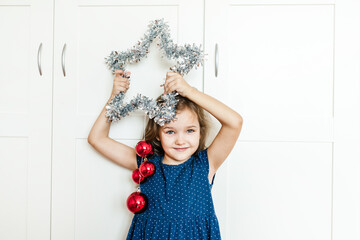 A girl holds a star in her hands to decorate the house for the new year and Christmas, the child is preparing for the holiday, helping parents, waiting for gifts