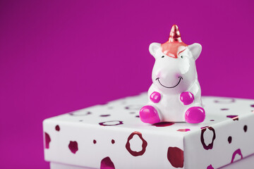 Figurine of a unicorn on the box with a gift on a pink background.