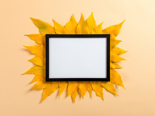 Frame and autumn leaves on a yellow background, mockup for design, place for text, concept of autumn. Copy space.