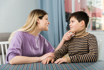 Portrait of young woman and son chatting at table indoors