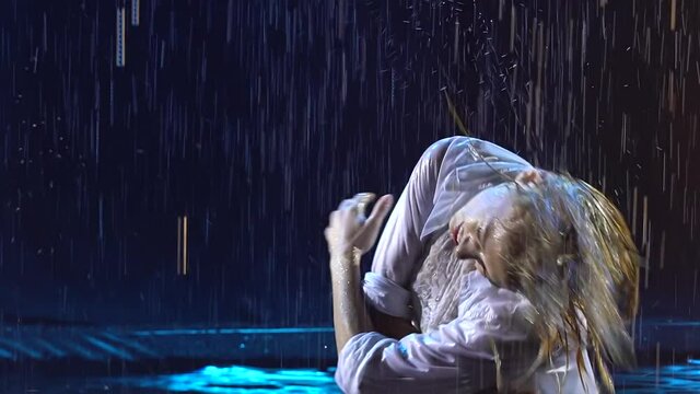 Two sexy beautiful women erotically move among the drops of rain and smoke. Dancers in wet clothes pose passionately in slow motion. Close up.