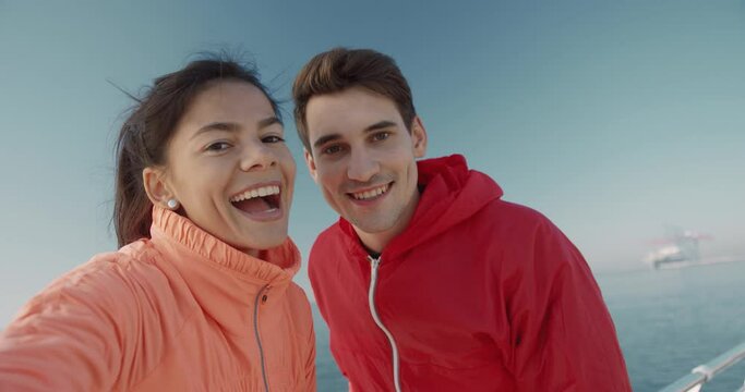 Young handsome guy and girl record video standing on the pier on background of blue sky and sea. Happy people smiling at camera and talking.