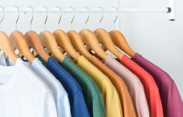 close up collection of colorful t-shirts hanging on wooden clothes hanger in closet or clothing...