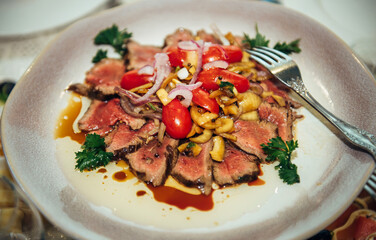 Warm salad with roast beef, pickled onions, cherry tomatoes and green parsley on a vintage plate, close-up. Stylish serving of dishes in the restaurant of European cuisine.