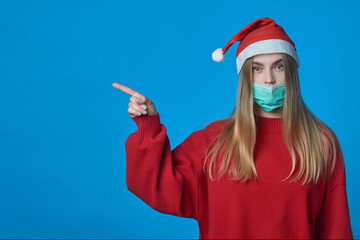 Fototapeta na wymiar Girl in a medical mask and Santa hat with a pointer