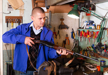 Qualified gun repairman examining smoothbore hunting shotgun before repair or preventive maintenance in workshop.