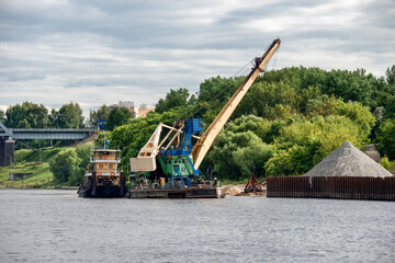 Crane and barge for sand on shore of Volga river at spring cloudy day