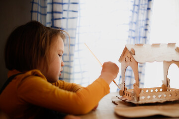 Caucasian girl kid with long hair colors bird feeder, winter bird care and children's creativity