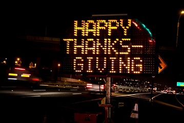 An electronic freeway sign stating Happy Thanksgiving with traffic in the background