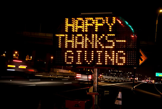 An Electronic Freeway Sign Stating Happy Thanksgiving With Traffic In The Background