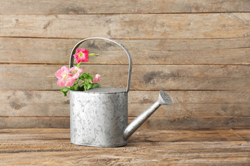 Watering can with flowers on wooden background