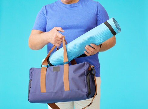 Sporty Senior Man With Bag And Yoga Mat On Color Background